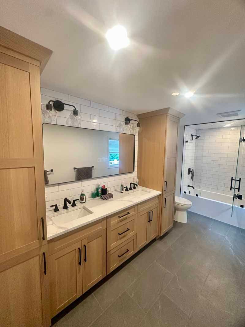 Bathroom with light wood cabinets, double sink, white tile, and gray flooring.