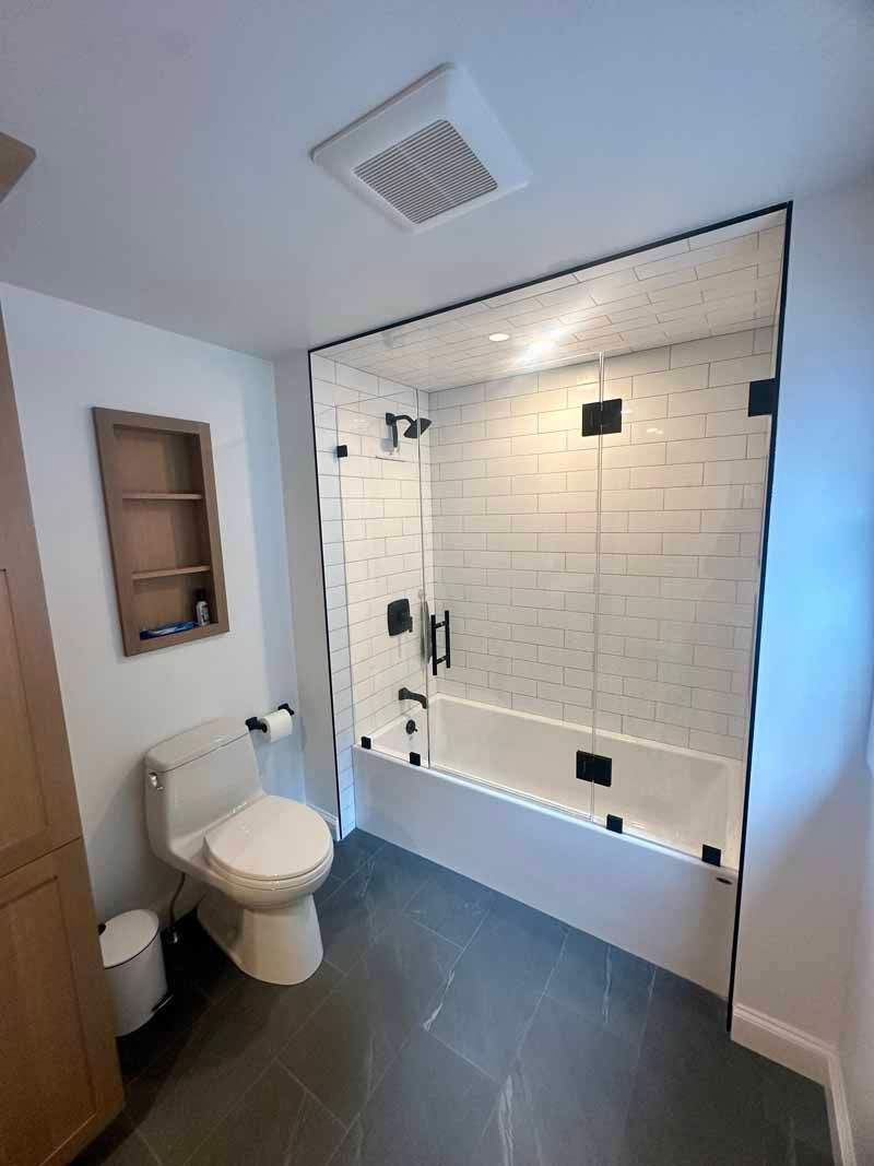 Modern bathroom with white and gray tile, glass shower enclosure, and a toilet.