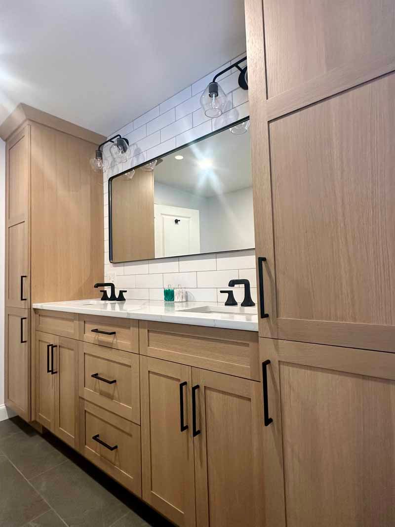 Bathroom with light wood cabinets, black hardware, white countertop, large mirror.