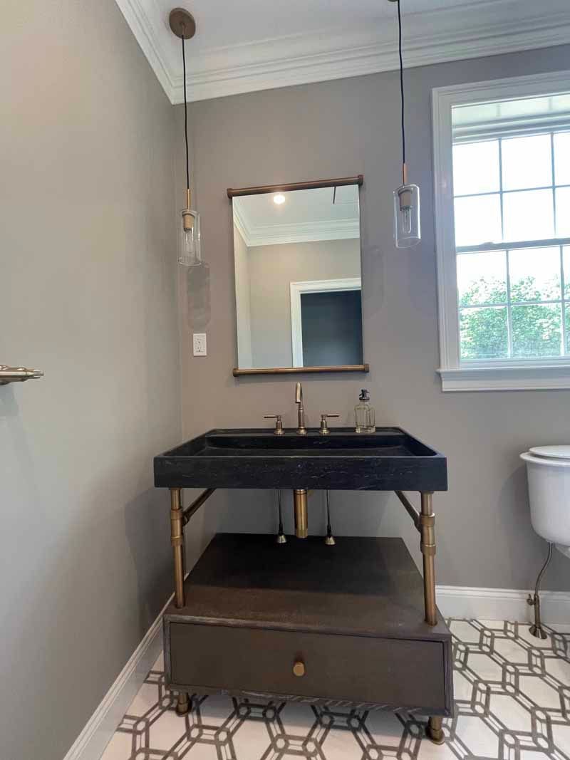 Bathroom with a gray wall, dark vanity with gold legs, mirror, pendant lights, and patterned floor.