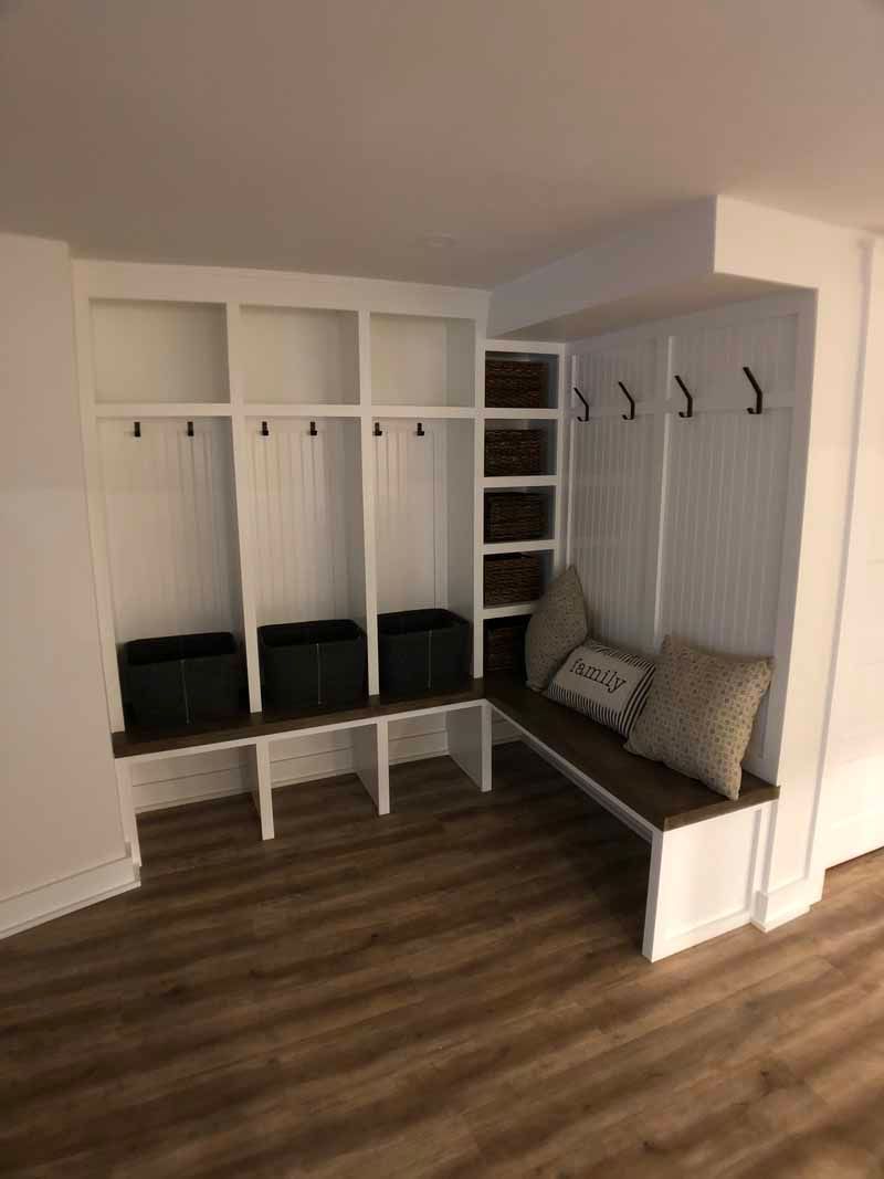 White built-in entryway storage with hooks, shelves, and bench. Includes storage baskets and decorative pillows.