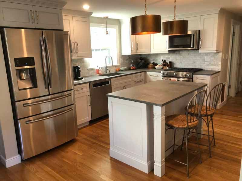 Modern kitchen with stainless steel appliances, white cabinets, and island with two stools.