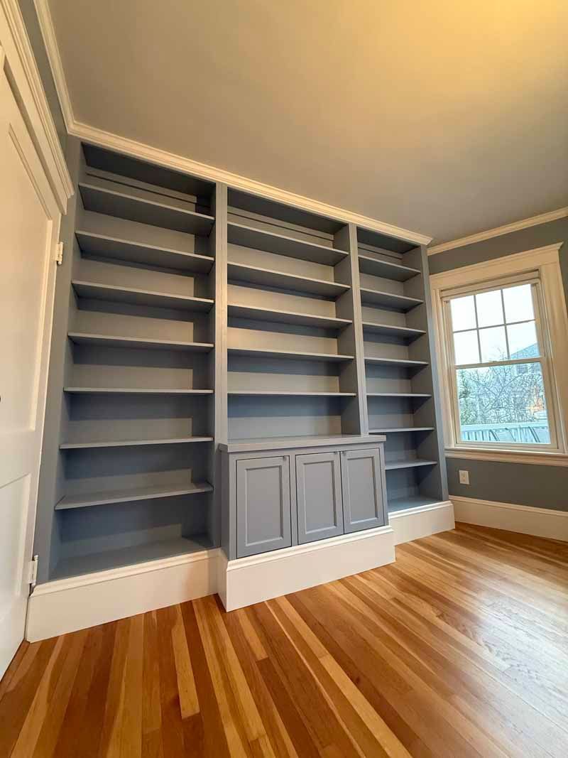 Built-in blue bookshelves with a cabinet and hardwood floor. Window to the right. White trim.
