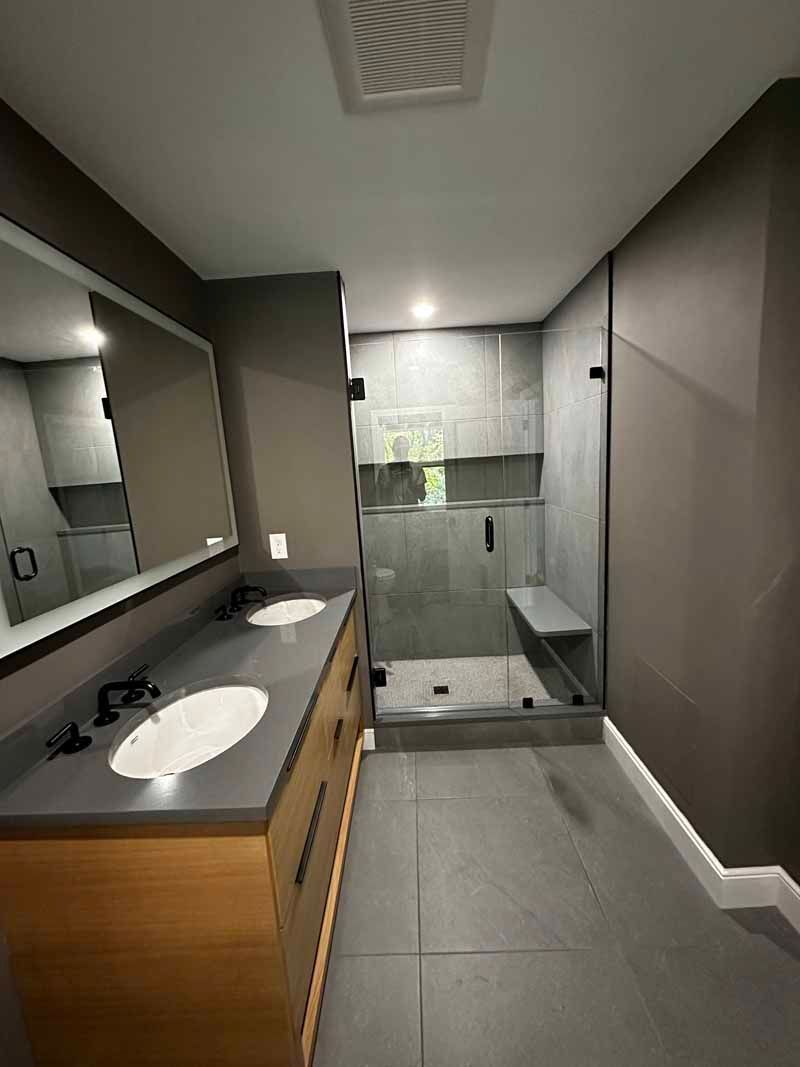 Modern bathroom with double vanity, gray tile, and glass shower.