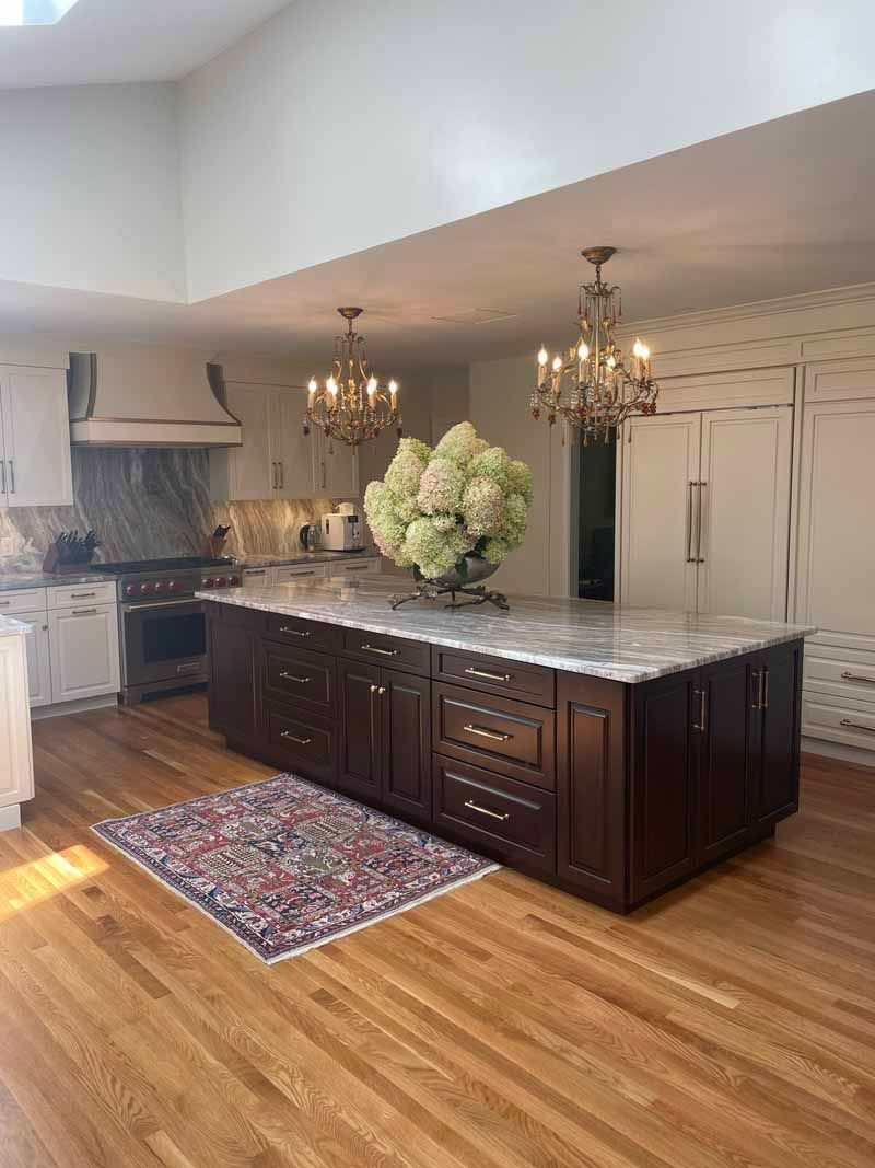 Elegant kitchen with wooden floors, island, chandeliers, and floral arrangement.