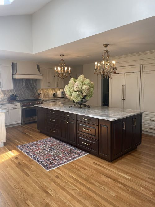 Kitchen with dark wood island, two chandeliers, hardwood floors, and a colorful rug.