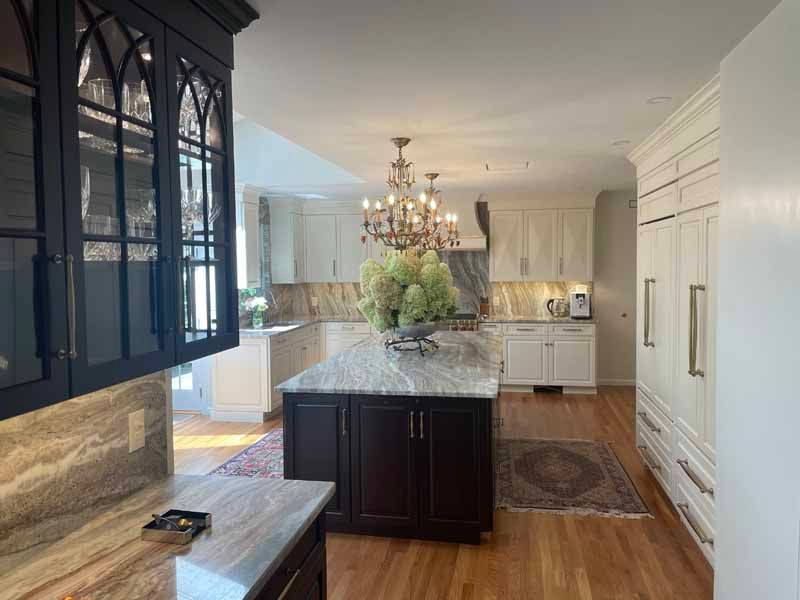 Elegant kitchen with white and dark cabinetry, granite countertops, and a central island with a chandelier.