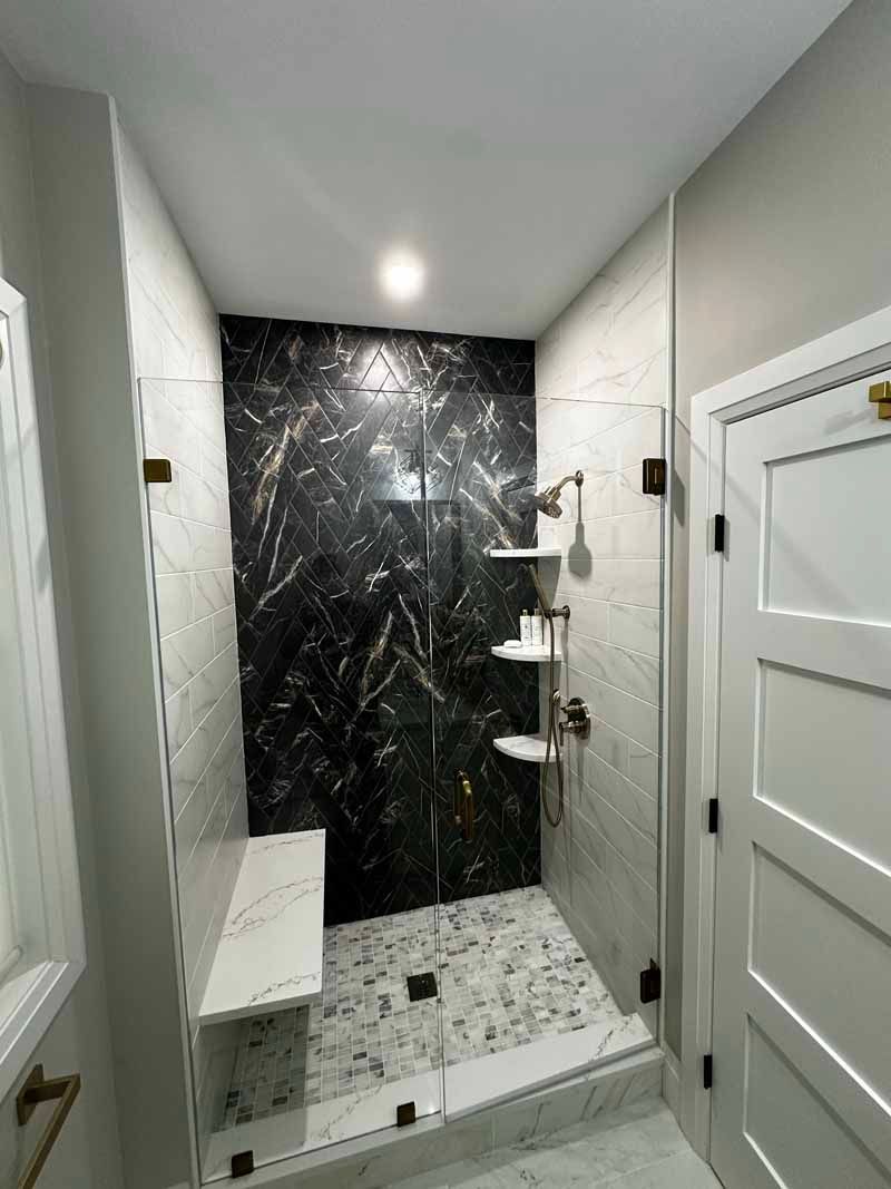 Modern shower with marble and black stone accent wall, bench, and shelves.