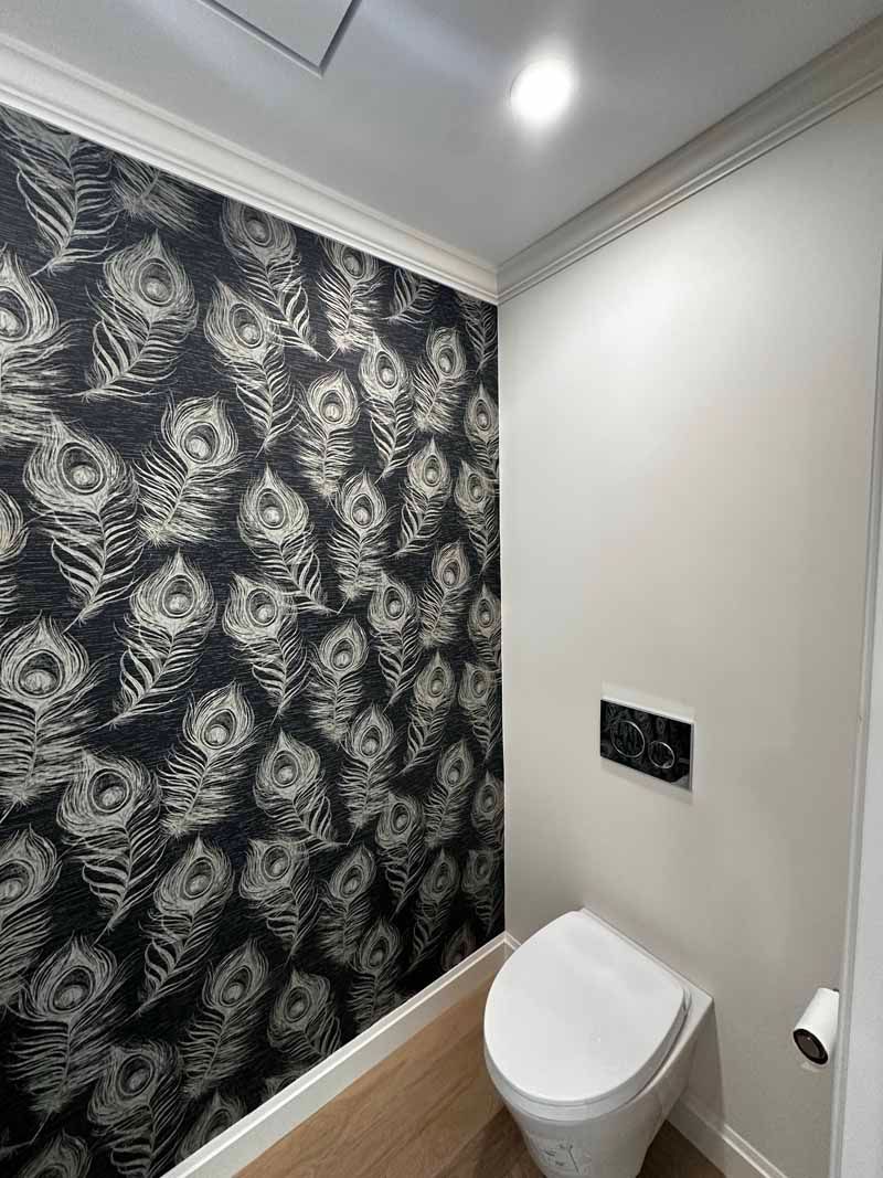 Small bathroom with a toilet and patterned wallpaper. White trim and walls.