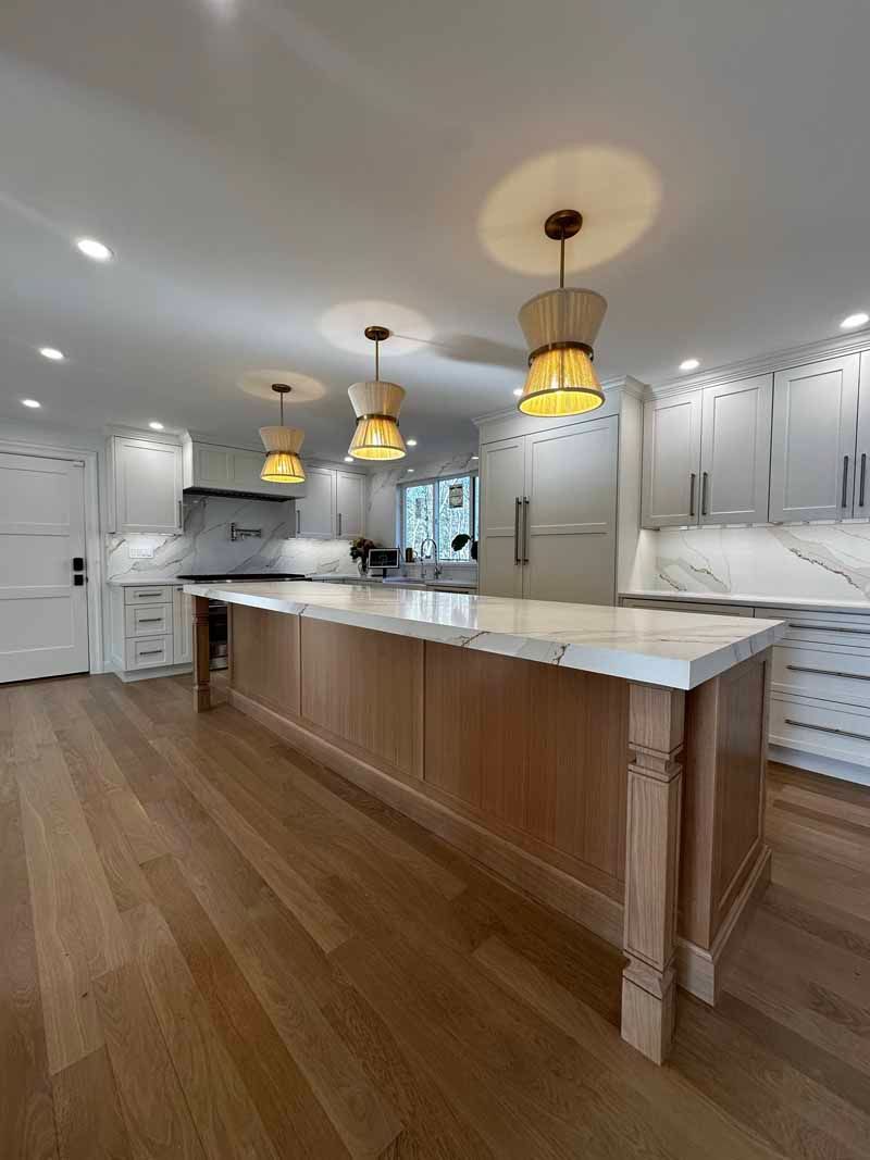Spacious kitchen with a light wood island, marble countertops, and three pendant lights.