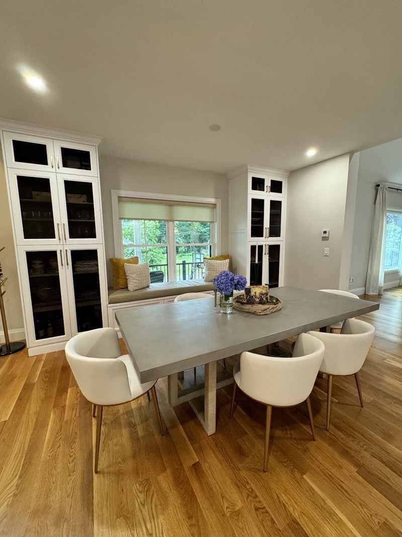 Dining room with a concrete table, white chairs, and built-in white cabinets. A window seat with pillows is included.