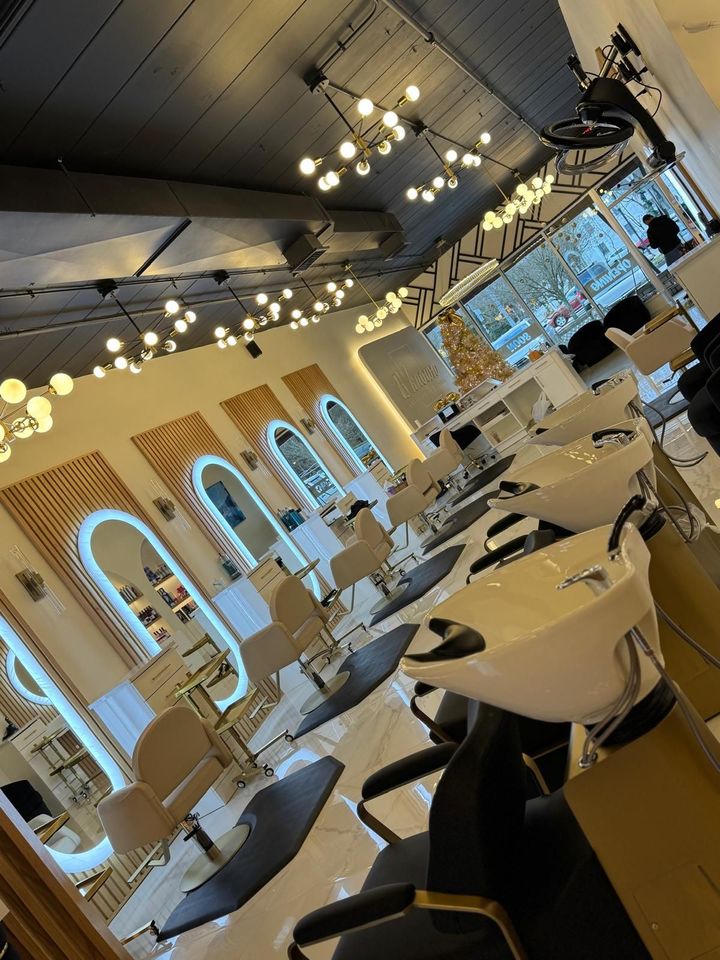 Interior of a hair salon with styling stations, mirrors, and washing stations. Neutral tones with warm lighting.