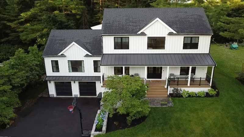 White farmhouse-style house with black roof, garage doors, and trim. Front porch, black asphalt driveway, and green lawn.