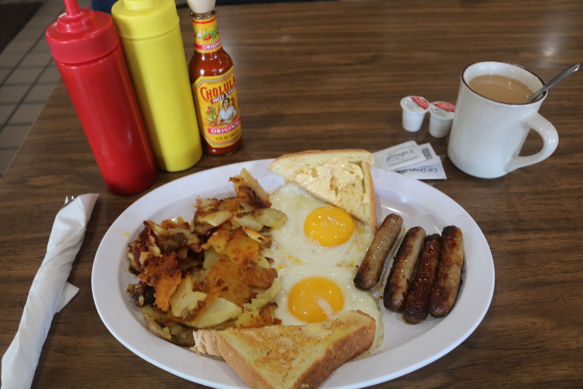 A plate of food with eggs , potatoes , toast and sausage on a table.