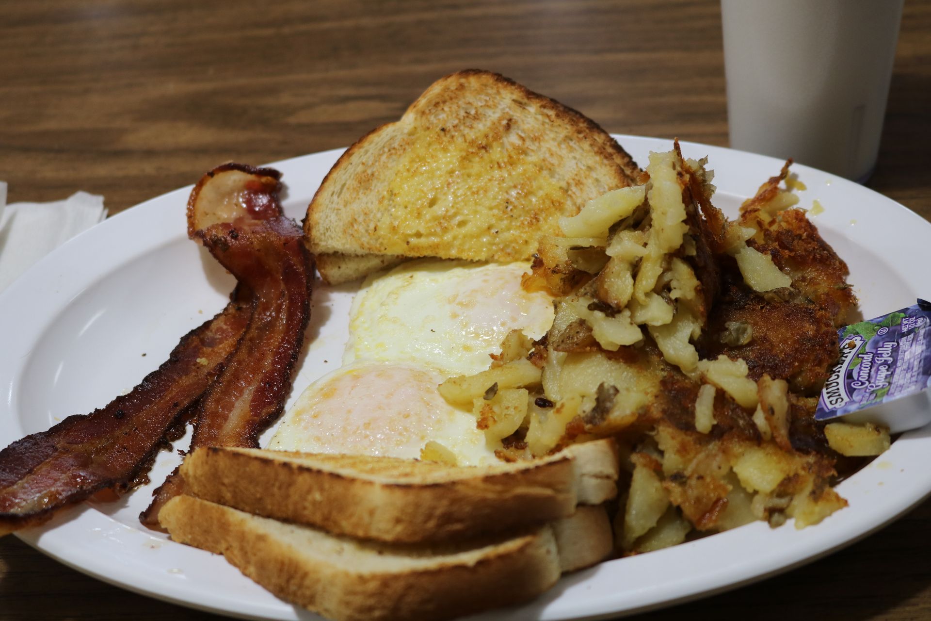 A white plate topped with eggs , bacon , toast and potatoes.