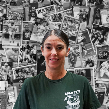 A woman wearing a spartan 's t-shirt is standing in front of a wall of football cards.