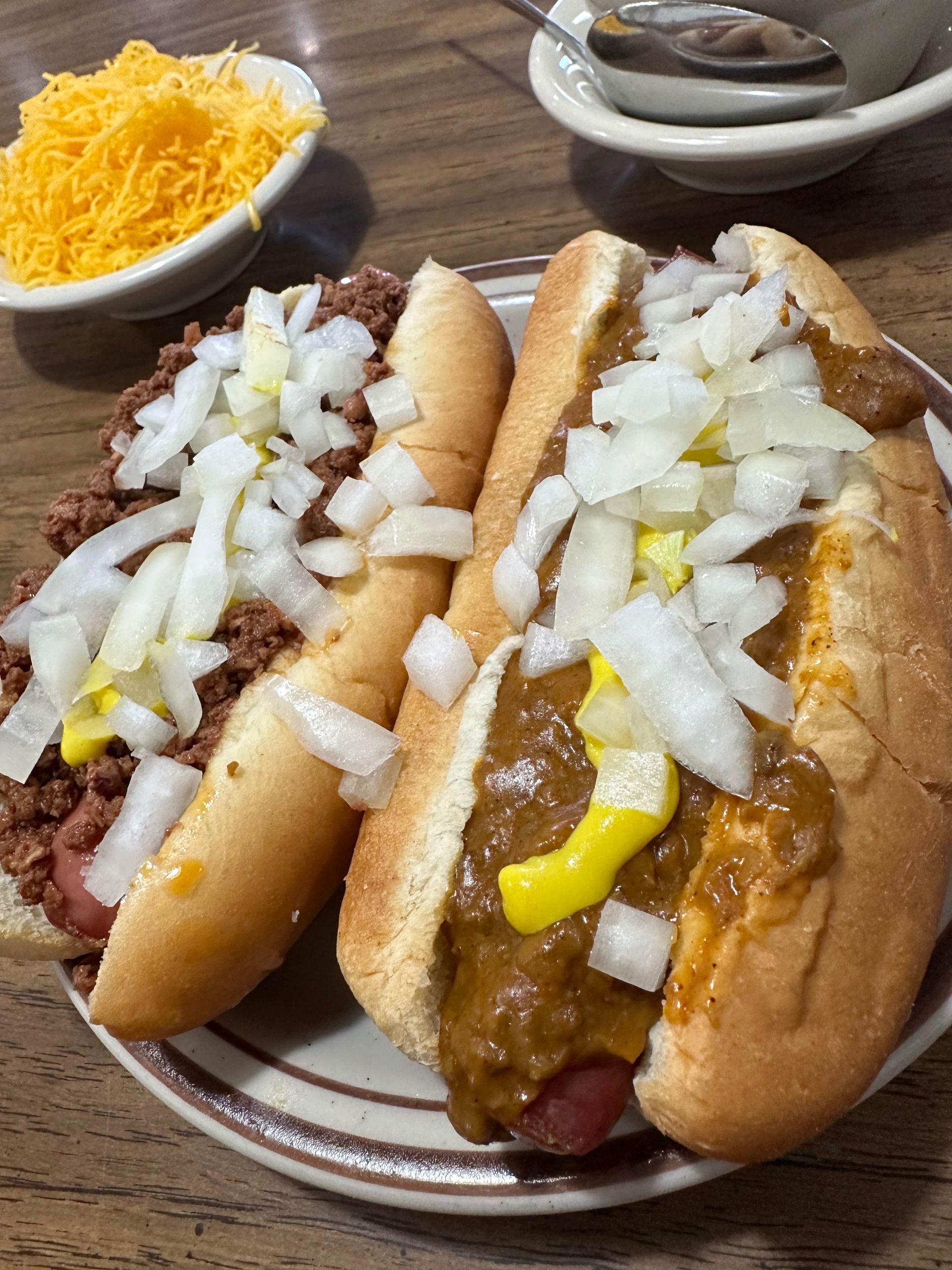 Two chili dogs with onions , mustard and cheese on a plate.