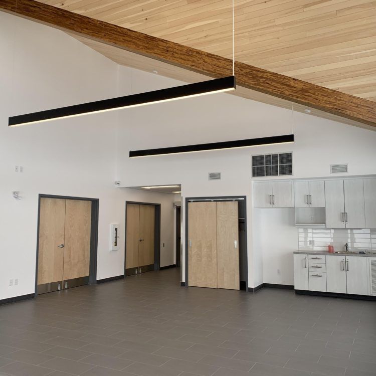 Pièce vide aux murs clairs, plafond en bois, plusieurs luminaires et une kitchenette.