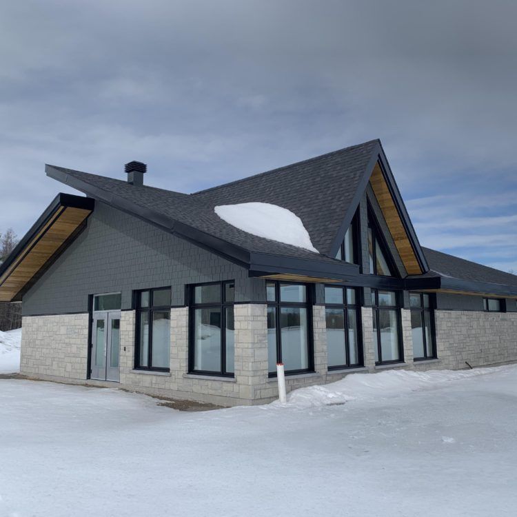 Un bâtiment moderne au toit sombre et aux grandes fenêtres, entouré de neige.