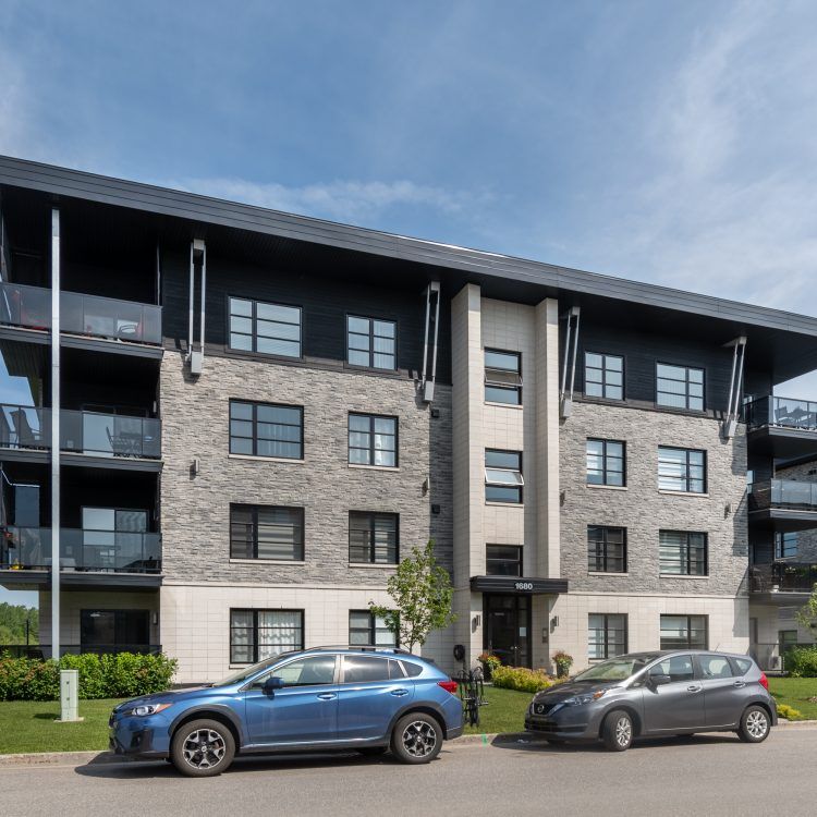 Immeuble d'appartements moderne avec deux voitures garées devant.