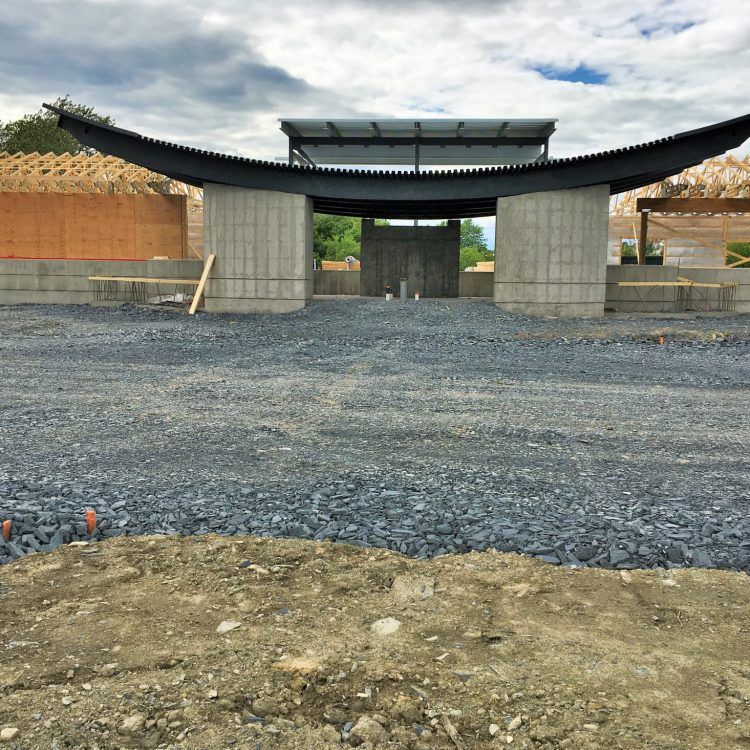 Chantier de construction avec une structure partiellement édifiée présentant un toit noir incurvé et des supports en béton.
