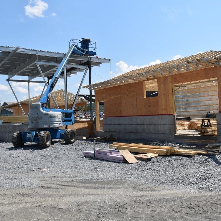 Chantier de construction avec une plateforme élévatrice bleue près d'un bâtiment partiellement construit à la charpente apparente en bois.