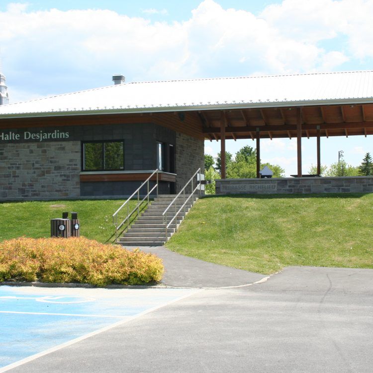 Bâtiment Halte Desjardins avec façade en pierre, toit en pente, escaliers et aire de pique-nique couverte.