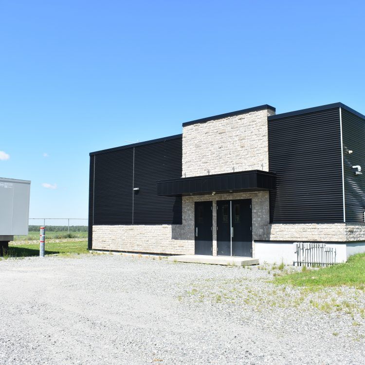 Bâtiment moderne avec bardage noir et éléments en pierre, double porte et parking en gravier.