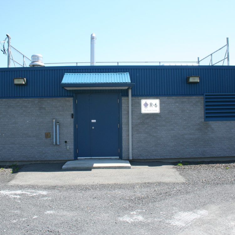 Bâtiment utilitaire bleu et gris avec une porte, un panneau « R-5 » et un petit auvent.