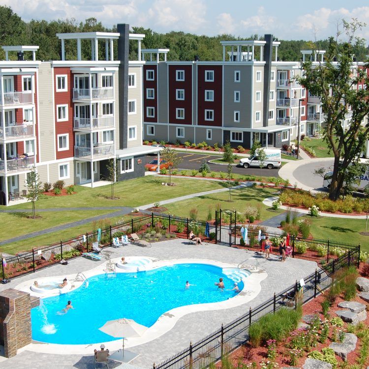 Complexe d'appartements avec piscine, des gens qui se baignent et une petite pelouse verte.