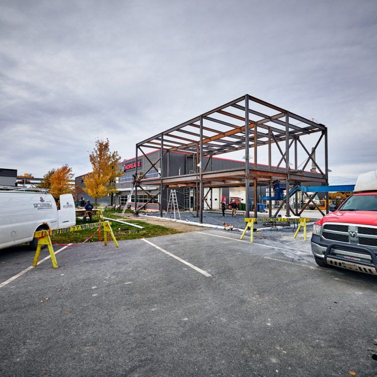Chantier de construction avec structure métallique ; parking, véhicules, ciel nuageux.