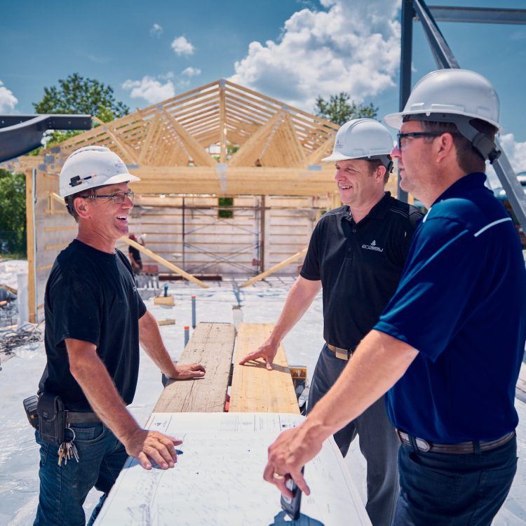 Trois ouvriers du bâtiment, casqués, discutent d'un plan sur un chantier.