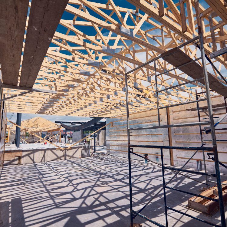 Chantier de construction avec charpente en bois, échafaudages et ombres projetées par le soleil.