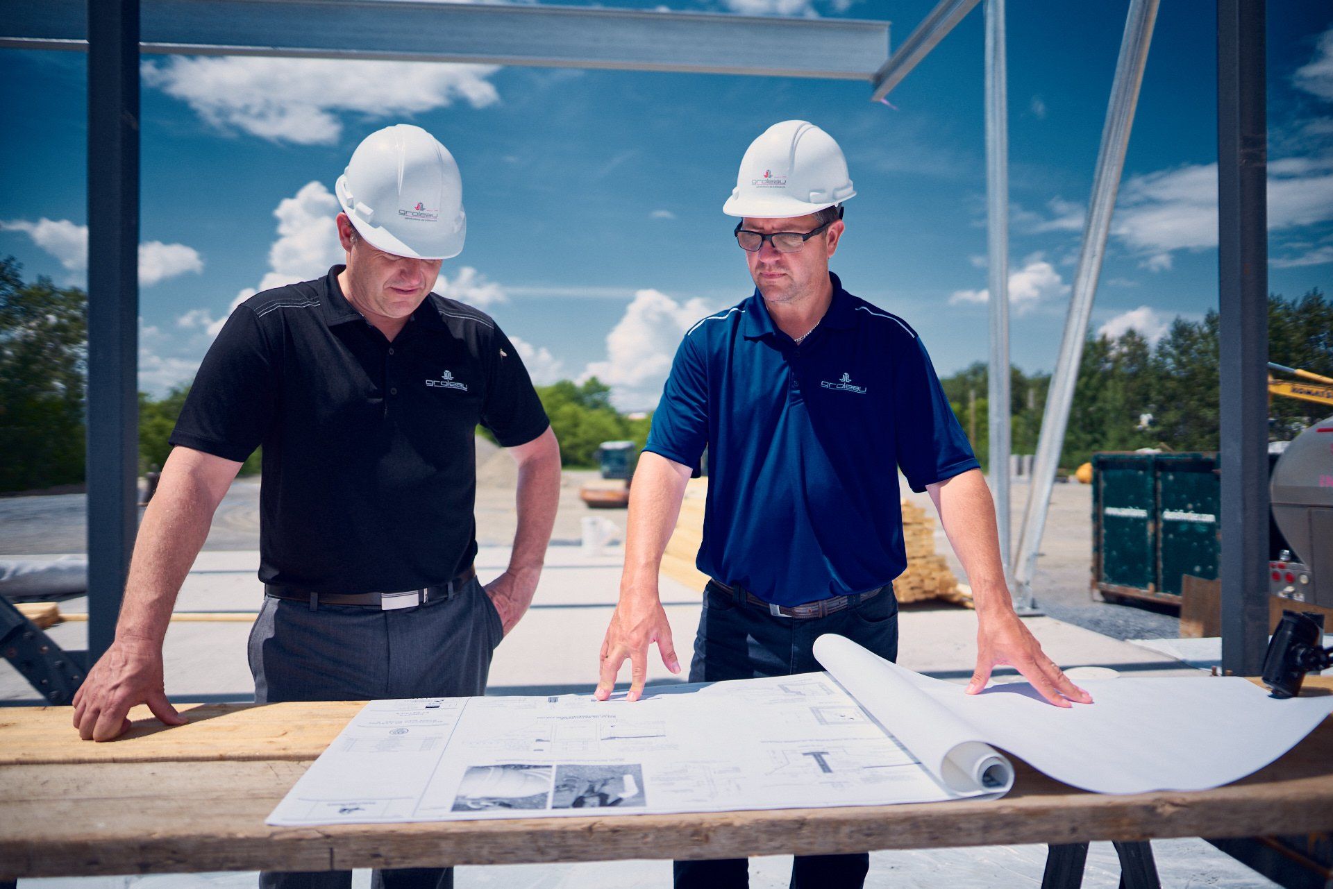 Deux hommes portant des casques de chantier examinent des plans sur un chantier de construction.