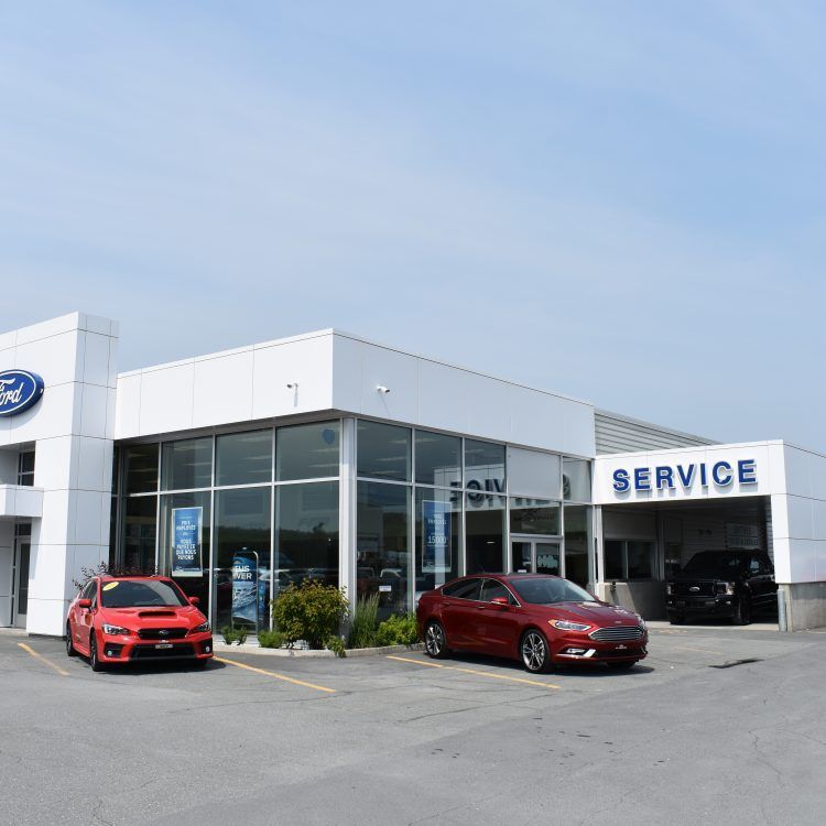 Concessionnaire Ford avec des voitures rouges et bordeaux garées devant le bâtiment. L'enseigne « Service après-vente » est visible.