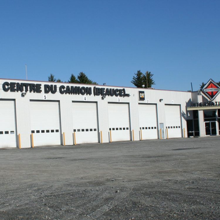 Extérieur de l'atelier de réparation de camions « Centre du Camion Beauce » avec ses multiples portes de garage sous un ciel bleu.