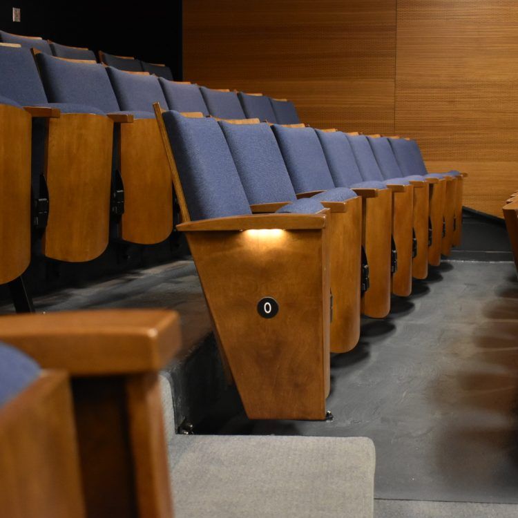Rangée de sièges de théâtre bleus rembourrés, numérotés et dotés d'accoudoirs en bois, dans un auditorium moderne.