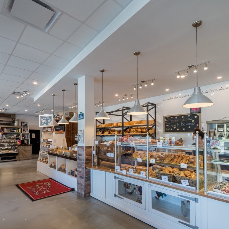 Intérieur d'une boulangerie avec des vitrines remplies de produits de boulangerie, un éclairage zénithal et des murs blancs.