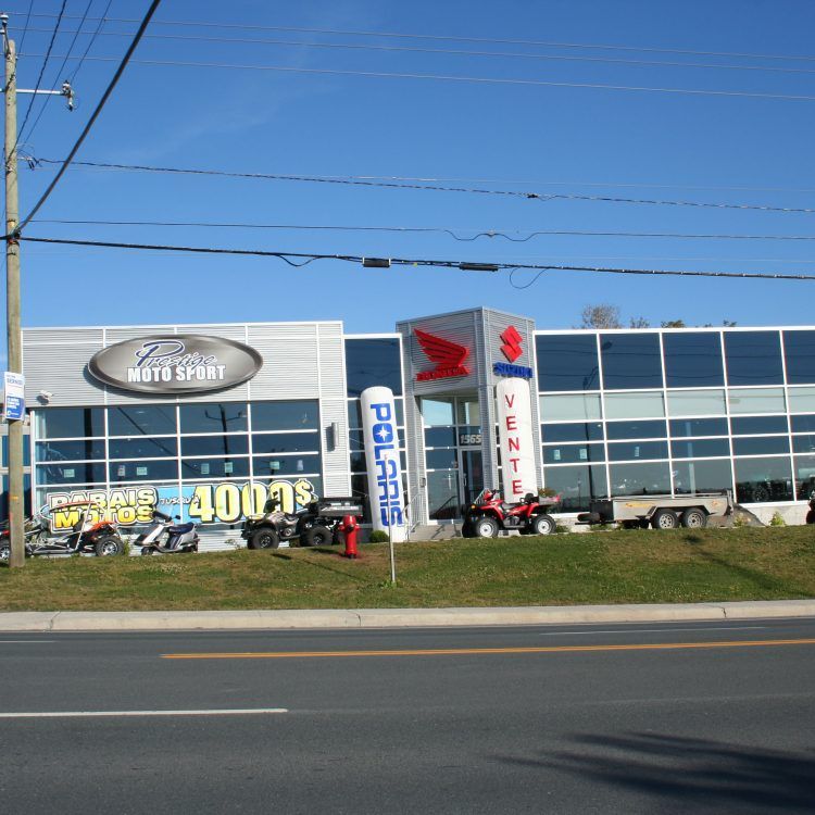 Concessionnaire de motos « Zone Moto Sport » avec logo Honda, véhicules exposés, ciel bleu dégagé.