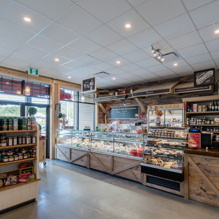 Intérieur d'une épicerie fine avec des vitrines présentant des aliments, des étagères de marchandises et une porte avec un panneau de sortie.