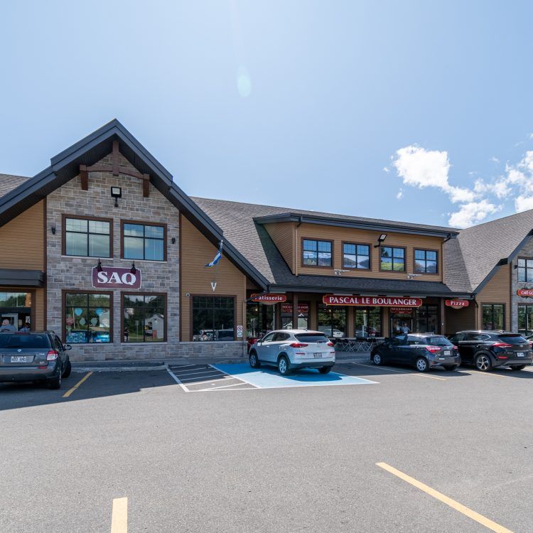 Vue extérieure d'un centre commercial abritant plusieurs commerces ; voitures garées devant par une journée ensoleillée.