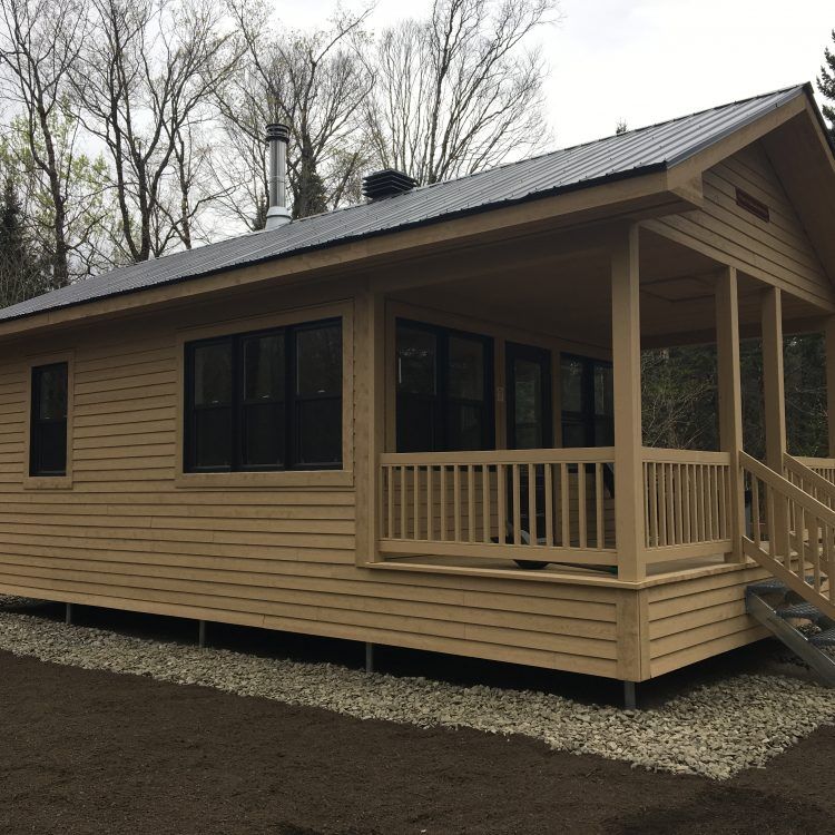 Cabane en bois clair avec véranda et fenêtres sombres.