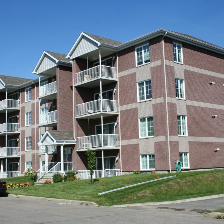 Immeuble d'appartements en briques de plusieurs étages avec balcons, pelouse et ciel bleu.