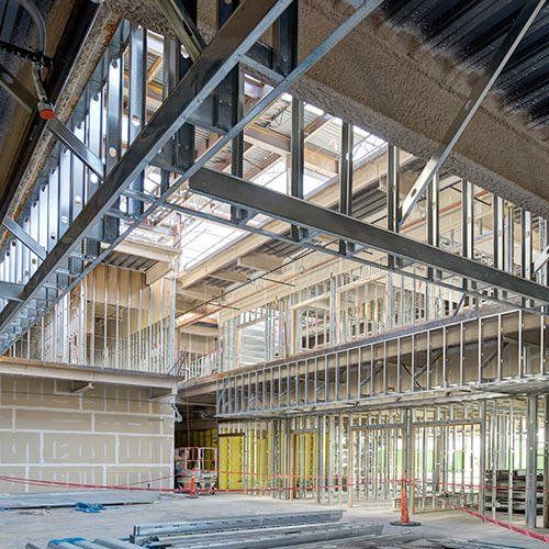 Intérieur d'un bâtiment en construction, montrant la charpente métallique et les murs inachevés.