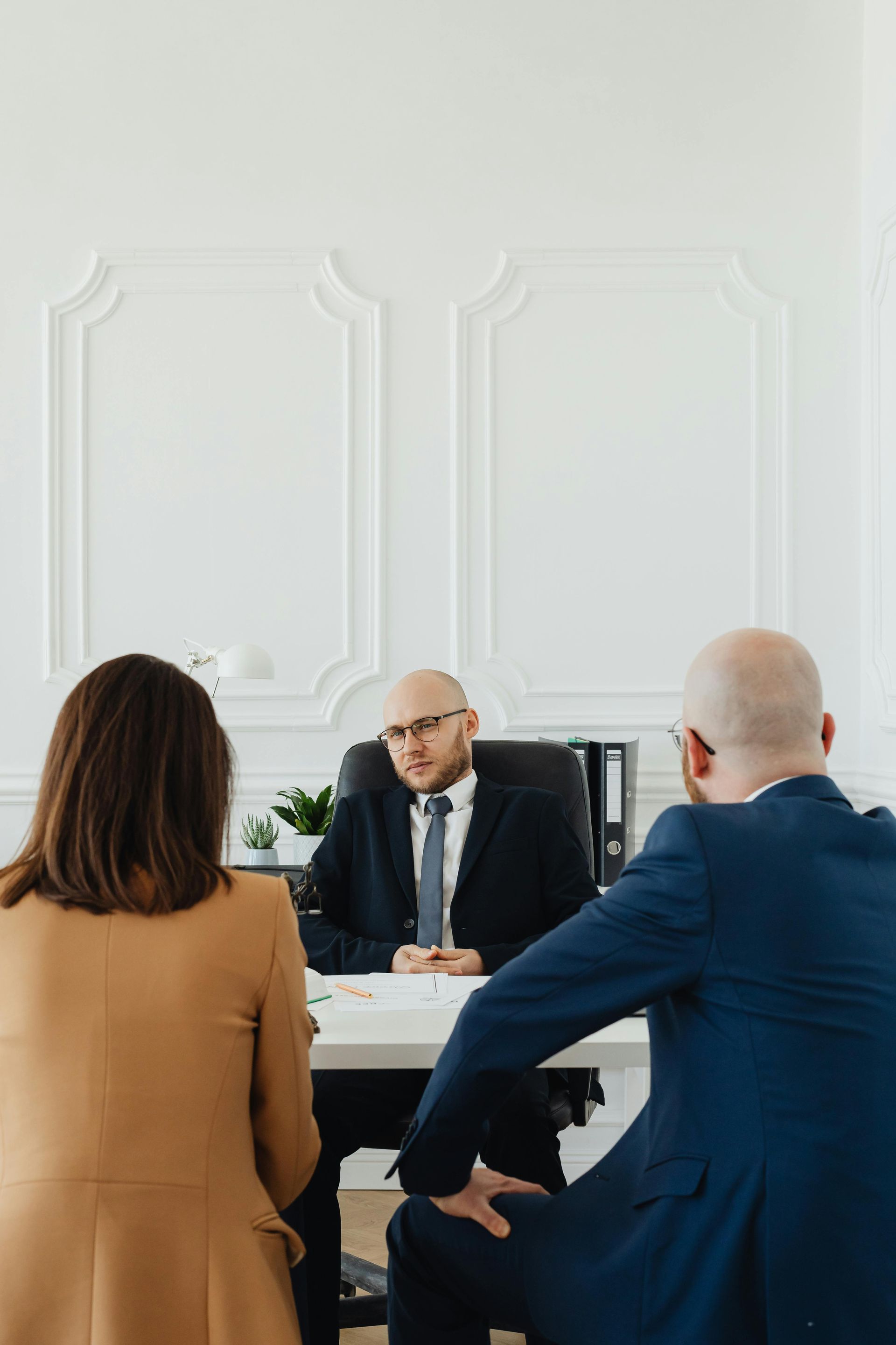 A man in a suit and tie is sitting at a desk with two people.