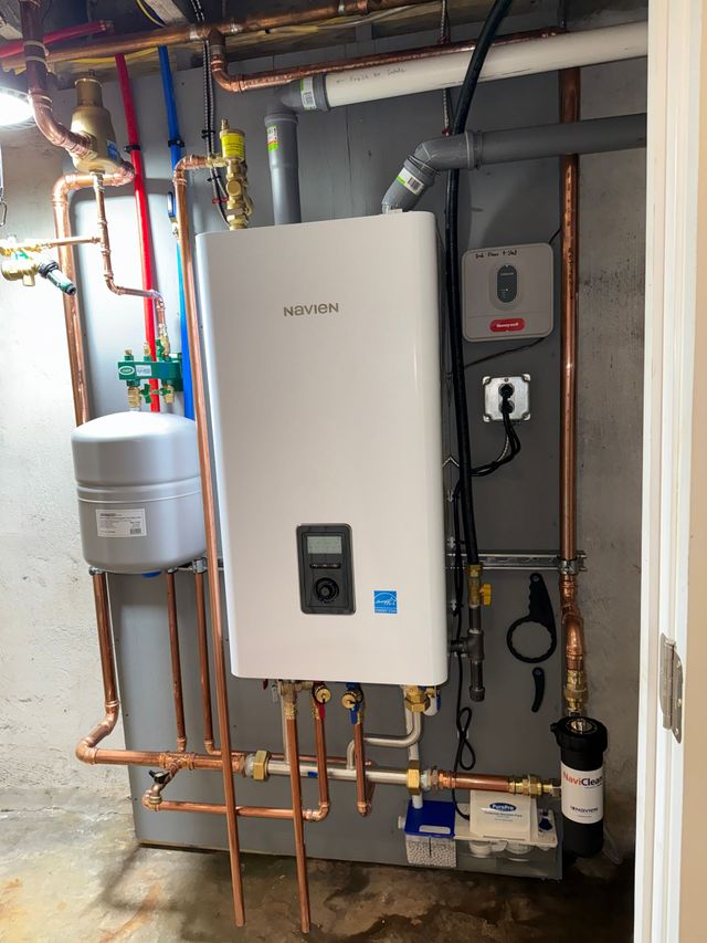 Wall-mounted tankless water heater with copper pipes in a basement setting.