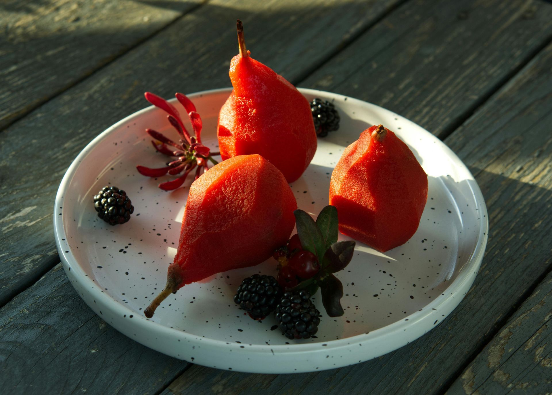 A white plate topped with red pears and blackberries