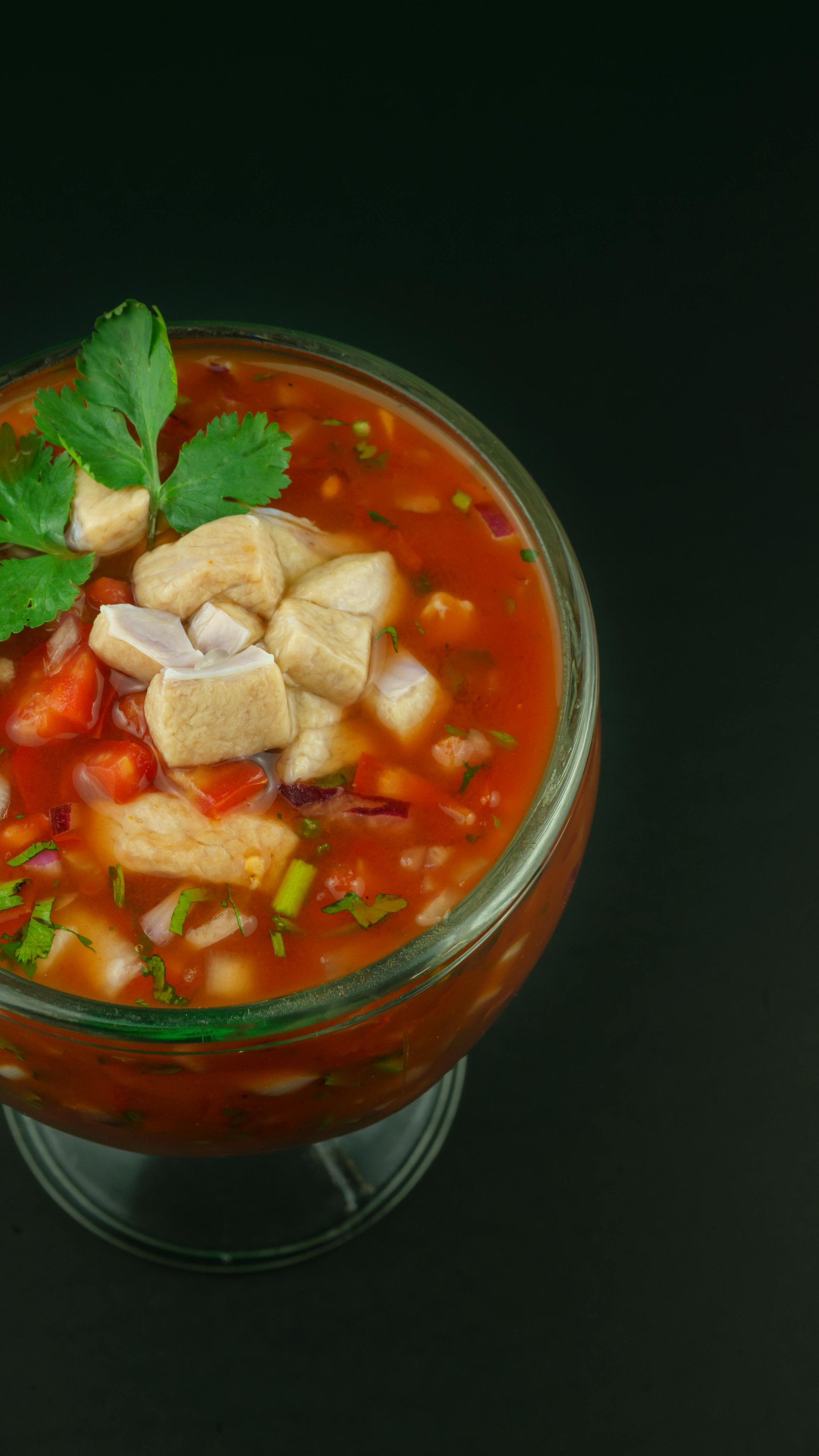 A close up of a bowl of soup with mushrooms and tomatoes on a black background.