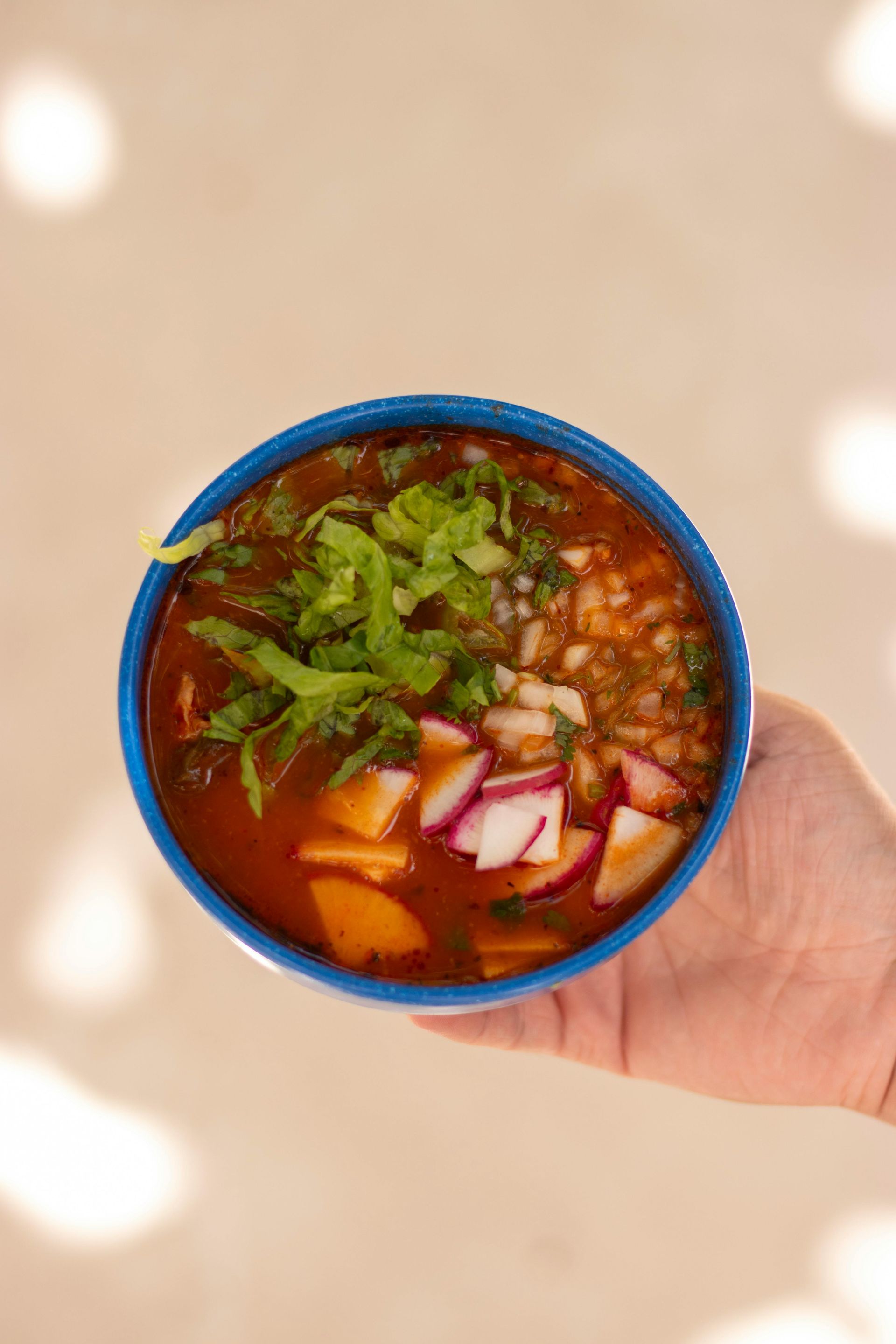 A person is holding a bowl of soup with vegetables in their hand.