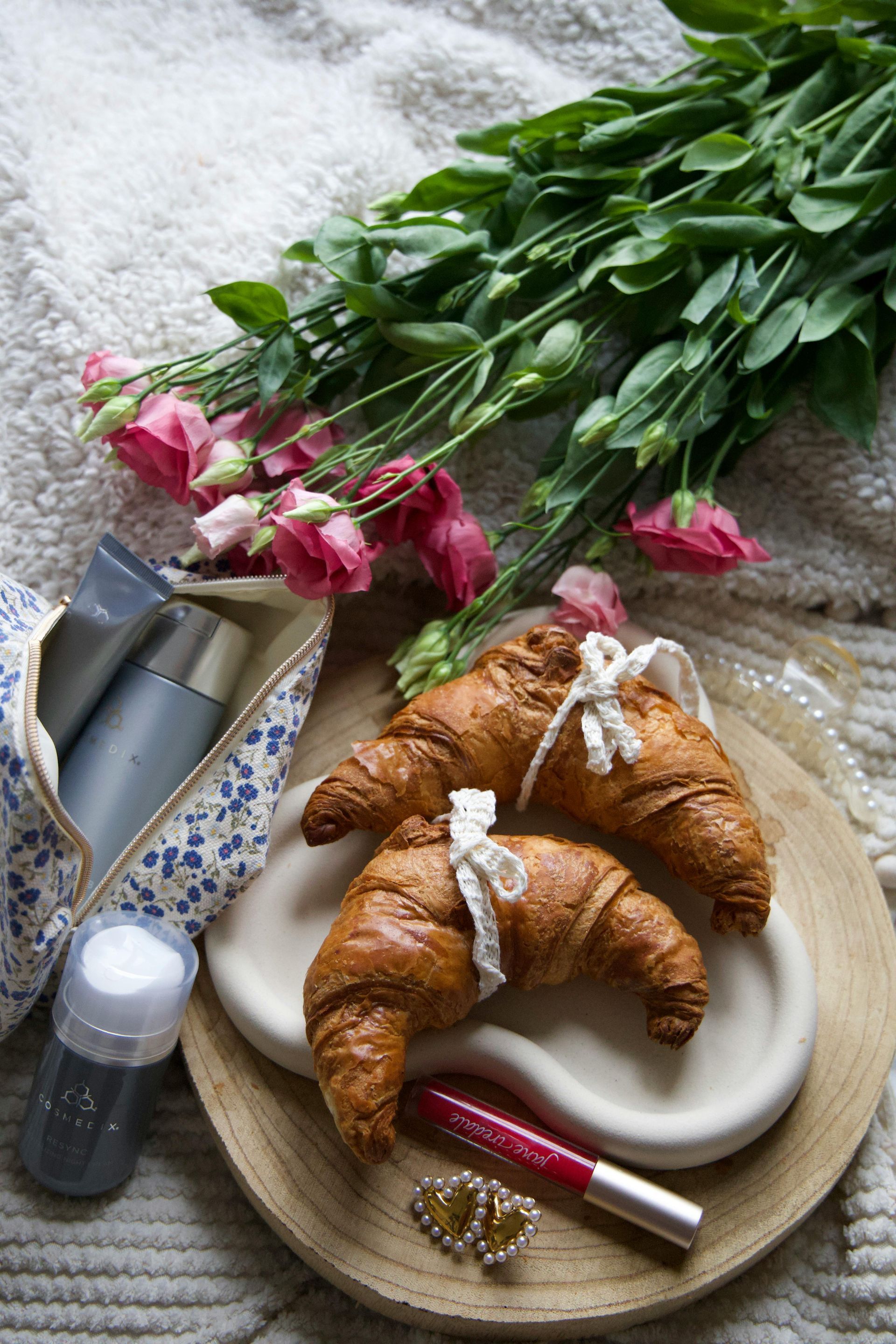 There are two croissants on a plate next to a bouquet of flowers.
